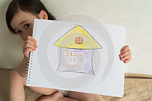 It is important to stay home during a pandemic. Coronovirus World Quarantine. Little girl holding a drawing in her hands