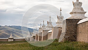 The imposing wall of an old monastery, consisting of white stupas and red bricks, in the hilly landscape of central