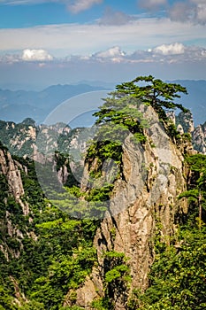 Impossibly steep rock with trees covering it and mountain ranges in the distance at Huang Shan in China