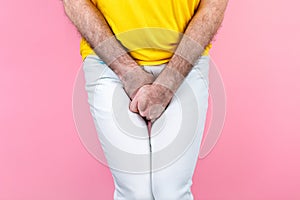 Impotence. A man in white jeans is holding his genitals with his hands, legs together. Pink background. Close up of hands. Copy