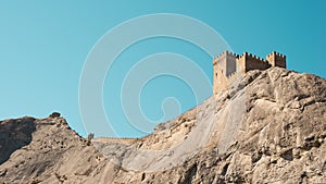 An impregnable fortress high on a cliff, lit by the bright sun.