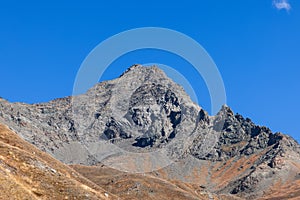 Impregnable granite black steep mountainside and sharp rocks with top peak under background of clear blue sky