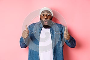 Impressed african-american hipster guy showing thumbs-up, approve and like offer, praising great choice, standing over