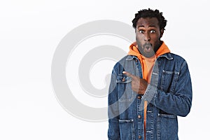 Impressed, astonished african-american bearded guy in denim jacket, orange hoodie, whistle from amazement, folding lips photo