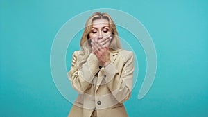 Impressed shocked adult blond woman in business style clothes closing mouth with hand, keeping silence, confused with secrets