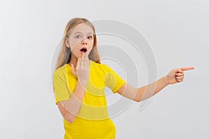 Impressed teen girl pointing finger right and looking amazed, showing advertisement, standing in blank yellow tshirt over white