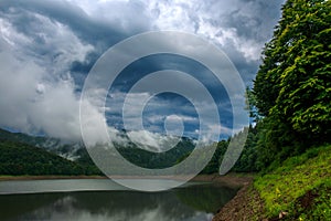 Impressive landscape of green coniferous mountains above lake against the background of stormy gray clouds, rainy weather, Ukraine