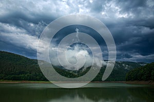 Impressive landscape of green coniferous mountains above lake against the background of stormy gray clouds, rainy weather, Ukraine