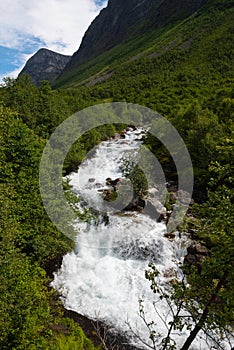 The impressive Storseterfossen StorsÃ¦terfossen with a path leading behind it throwing water down towards Geiranger