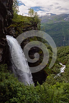 The impressive Storseterfossen StorsÃ¦terfossen with a path leading behind it throwing water down towards Geiranger