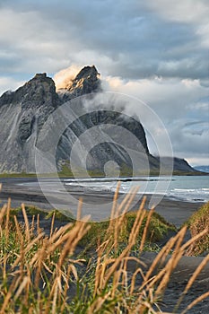 Impressive view of black sand beach in Iceland and epic Vestrahorn mountains in cloudy weather. Calm, cold ocean waves