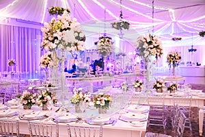 IMPRESSIVE VIOLET RECEPTION VENUE WITH BEAUTIFUL FLORAL GREEN DECORATION,  WHITE TABLES, BLURRED BACKGROUND, YELLOW LIGHTS, AND BL