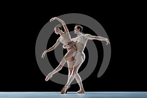 Impressive young man and woman, talented, professional dancers performing ballet art against black studio background