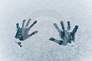 Imprint of two palm hands on the white snow texture. Two human handprints on frozen dark blue glass background. Concept of winter