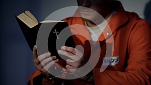 Imprisoned man in handcuffs reading bible, feeling guilty and praying for soul