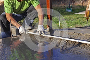 Improvement of the yard, a man evens out the concrete mortar with the rule