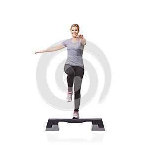 Improving her health one step at a time. A smiling young woman doing aerobics on an aerobic step against a white