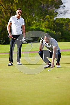 Improving their handicap one ball at a time. two golfers watching as the ball approaches the hole.