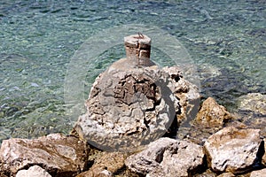 Improvised homemade stone mooring bollard with rusted metal hook on top built on top of large rock formation