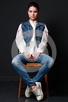 Impudent brunette woman in jeans vest sitting on the chair