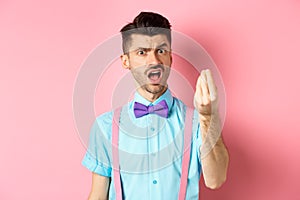 Impulsive young man having an arument, prove someone wrong, showing italian gesture and complaining, standing over pink