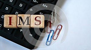 IMS - acronym on wooden cubes against the background of a calculator and paper clips. Copy space