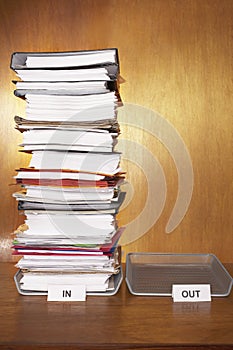 Inbox with stack of paperwork empty outbox on desk photo