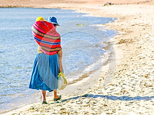 Incan woman with baby in the colorful scarf on a back. Walks on the beach of Island of the Sun at Titicaca Lake, Bolivia