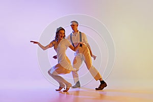 Incendiary dance. Emotional couple of dancers in retro style outfits dancing social dances isolated on gradient lilac