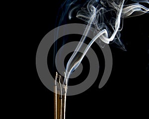 Incense sticks are burning on the black background. The smoke during incense sticks burning for make merit. Buddhists make merit,