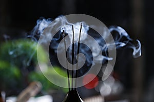 Incense sticks smoldering in holder on blurred background, closeup