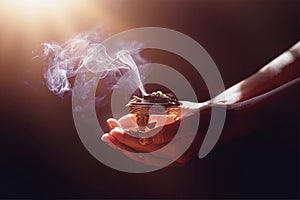 incense in a woman hand, incense smoke on a black background.