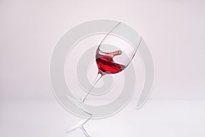 inclined wineglass with splashing delicious red wine on reflective surface