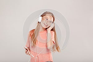 Inclusive Beauty. Girl with freckles in headphones standing isolated on grey holding smartphone listening music smiling