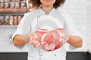 Incognito female butcher showing meat in supermarket.