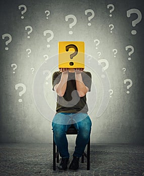 Incognito young man seated on a chair holding a yellow box with question mark instead of head