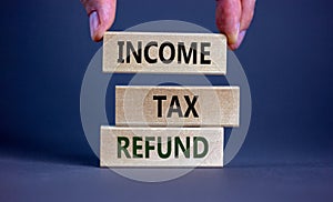 Income tax refund symbol. Wooden blocks form the words `Income tax refund` on grey background. Male hand. Business and income ta