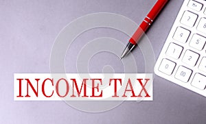 INCOME TAX text written on a gray background with pen and calculator