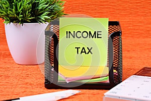 INCOME TAX text written on a green sticker next to office supplies on an orange background