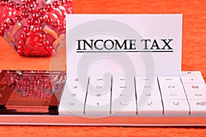 INCOME TAX text written on a white business card on a calculator on an orange background