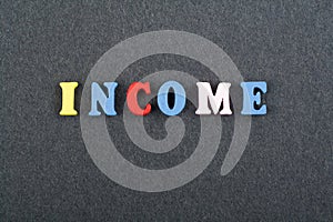 INCOME word on black board background composed from colorful abc alphabet block wooden letters, copy space for ad text. Learning