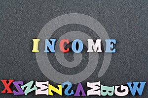 INCOME word on black board background composed from colorful abc alphabet block wooden letters, copy space for ad text. Learning