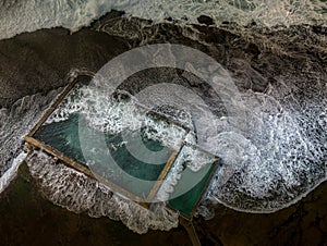 Incoming tide waves crash over the rock pool at Mona Vale