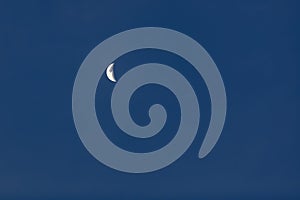 Bright white crescent moon against a cloudless blue sky