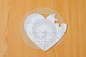 Incomplete heart shape jigsaw puzzle on wooden background