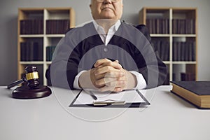 Incorruptible senior judge sitting at table with gavel and case papers in court of law photo