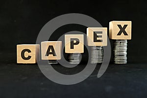 Increase in capex or capital expenditure concept. Wooden blocks with increasing stack of coins in black background.