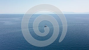 Incredible aerial shot in the open sea with a view of a white boat sailing in Aegean Sea, Greece.