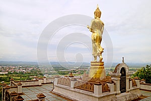 Golden Buddha image in walking posture overlooks the town of Nan, Wat Phra That Khao Noi temple in northern Thailand