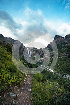 An incredible view of a majestic Shdugra waterfall in the distance, high in the Caucasus Mountains, rocky slopes, a rushing stream